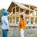 engineer discussing with a woman the project near a wood-framed house structure on a construction site