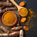 Turmeric roots and powdered turmeric next to each other on a black surface