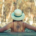 A woman with a straw hat and a tattoo on her back sitting on a bench