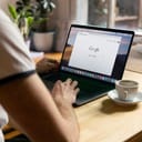 man using an Apple MacBook in a café and browsing the Google website