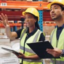 women and a man using their tablets to discuss logistics among cargo boxes in a warehouse