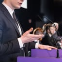 Close-up of a young formally-dressed man giving a public speech in a conference room