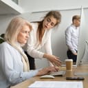 Young team leader correcting offended senior employee working on computer in office, female manager scolding aged old worker for mistake or incompetence, different generations and age discrimination
