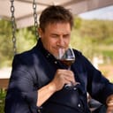 Man sitting in a garden with a glass of red wine in his hand, savoring and tasting it in an authentic, serene moment.