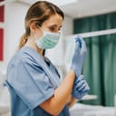 A female nurse wearing a facemask adjusting her sanitary gloves