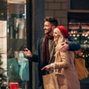 A laughing couple with shopping bags looking inside a shop