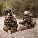 two soldiers in camouflage gear aiming rifles, prepared to shoot during a military operation or training