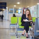 Young elegant business woman with hand luggage in international airport terminal, reading a book while waiting for flight