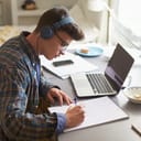 Teenage boy with headphones studying at a desk in his bedroom with his laptop in front of him