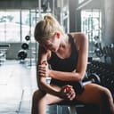 Woman in gym painfully holding her arm with a dumbbell resting on her leg