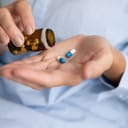 A closeup of a person taking two pills from a medicine bottle