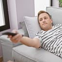 young man lying on the couch, flipping through TV channels at home