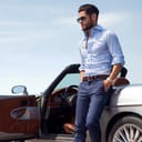 A man in a shirt and pants leaning on a convertible car