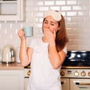 sleepy woman in the kitchen yawning and holding a coffee mug in her hand