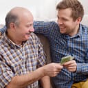 Close-up of an older father giving money to his adult son, providing financial assistance.