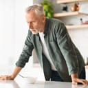 upset senior man leaning on a kitchen table with a white bowl in front of him, looking away deep in thought