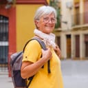 Portrait of senior traveler woman carrying backpack visiting the old town of Seville, smiling elderly lady enjoying travel and discovery