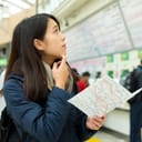 young woman at a train station confused while searching for the right direction with map in her hands