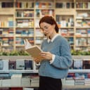 Concentrated young woman with glasses reading a book amidst the colorful collection of a well-stocked bookstore.