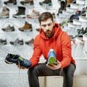 Man choosing trail shoes for hiking sitting in the fitting room of the modern sports shop