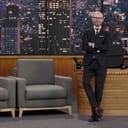 Late-night talk show host is leaning against his table in studio.