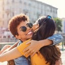 Happy meeting of two friends hugging in the street. Smiling girls friends laughing and hugging in the city centre. Multiethnic young women embrace each others after long time they have been distant.