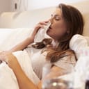 Sickly woman lying in bed holding a tissue over her mouth