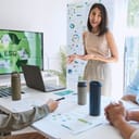 A young businesswoman leading a meeting, presenting ESG principles via a laptop connected to a monitor.