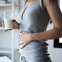Woman holding a glass of milk resting the other hand on the stomach