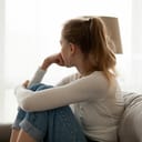 a young woman sitting on a couch at home and looking out the window