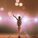 Back view of boy with hands up standing in stage lights