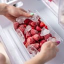 A person taking a plastic container with frozen strawberries from the freezer
