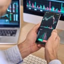 Over-the-shoulder view of a crypto trader using a smartphone app to examine stock market, close-up on the phone