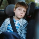 A little boy sitting in a car seat with a seatbelt on, feeling nauseous