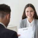 A girl smiling as she is being interviewed for a job. The interviewer is holding her resume.