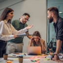 A stressed female office worker holding her head during a business meeting, while colleagues discuss issues that need resolution.