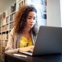 A young woman in a library working on a laptop