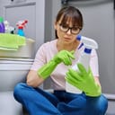 woman examining the label of a spray cleaner, reading instructions while seated on a bathroom floor