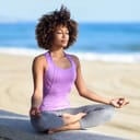 A woman in sports attire meditating at the beach