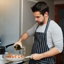 young man in an apron preparing dinner in his kitchen with white wine