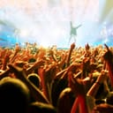 A crowd at a concert with their hands in the air and band playing in the background