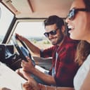 A happy young couple sits in the car, smiling as they use a map to navigate during their road trip.