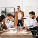 Female manager angrily talking to a group of unenthusiastic colleagues seated at table