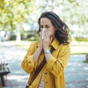 young woman blowing her nose in a park, allergies season
