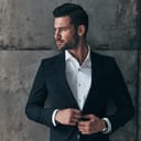 Charming man. Handsome young man in suit looking away and adjusting his jacket while standing indoors