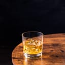 A glass of whiskey on rocks on a wooden table