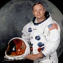 Portrait of Astronaut Neil A. Armstrong, commander of the Apollo 11 Lunar Landing mission in his space suit, with his helmet on the table in front of him. Behind him is a large photograph of the lunar surface.