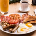 A traditional English breakfast with eggs, beans, sausages, bacon, tomatoes, mushrooms and toast, with an orange juice and a cup of coffee