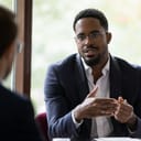Confident concentrated African American male employee talk with colleague explain thought or idea, focused biracial businessman speak with coworker or partner, brainstorm at office boardroom meeting