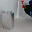 close-up of a gallon of paint thinner beside an old wall, with a painter clearing sticky residue in the corner